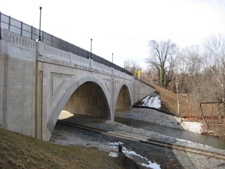 A bridge going over rail tracks and a small river