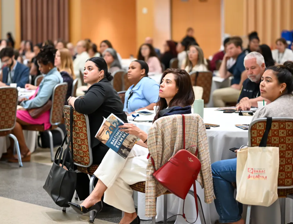 Summit participants are seated and listen to a speaker in a ballroom