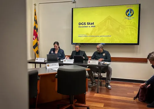 Three people sit at a table with a slideshow behind them