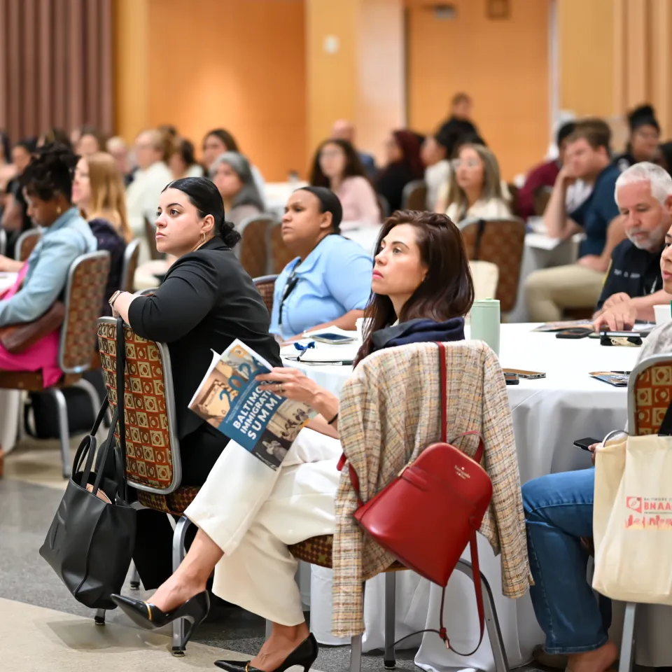 Summit participants are seated and listen to a speaker in a ballroom