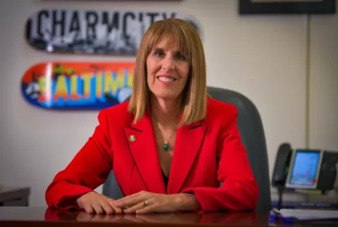 Image of the Inspector General Cumming in red blazer at desk