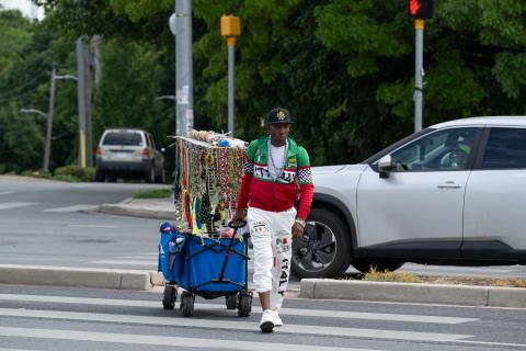 man dressed colorfully, pulling a cart of items to sell at an event