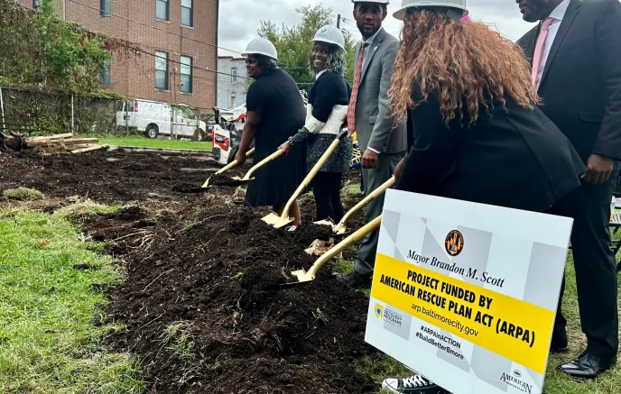 ARPA BCRP Playground Rebuild. A group of people in helmets participating in a groundbreaking ceremony with shovels. A sign in the foreground displays information about the project, indicating it is funded by the American Rescue Plan Act (ARPA). 