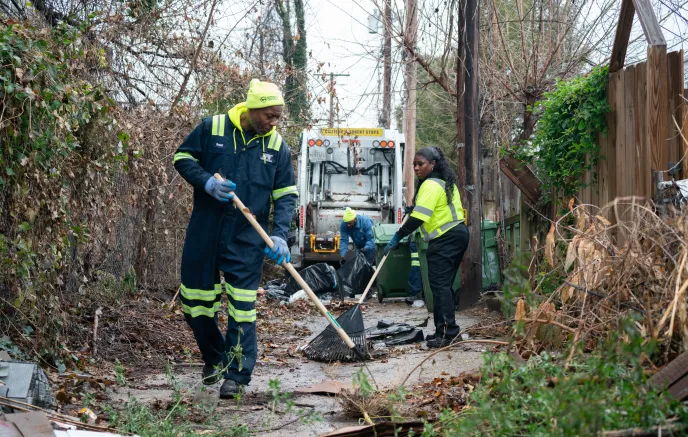 Three sanitation workers cleaning an alleyway together 