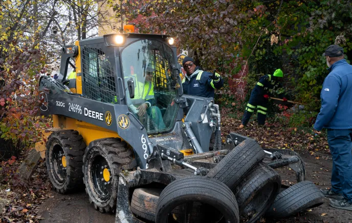 Department of Public Works employee collecting discarded tires from the ground with a loader vehicle 