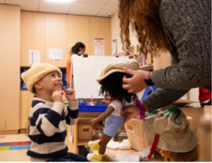 Educator handing a doll to a young child in a classroom