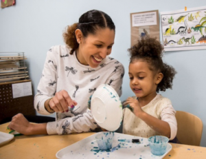 Educator and young child painting together