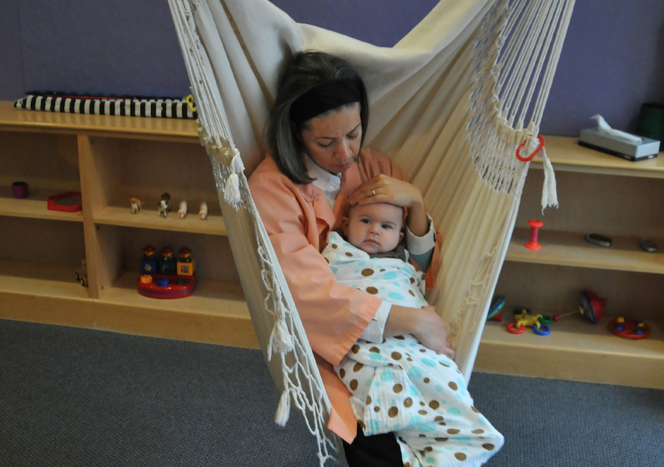 Adult holding baby in classroom hammock