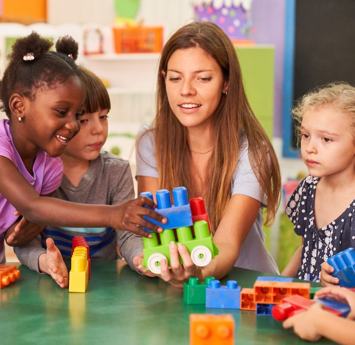 Young children and a teacher at a table with colorful blocks