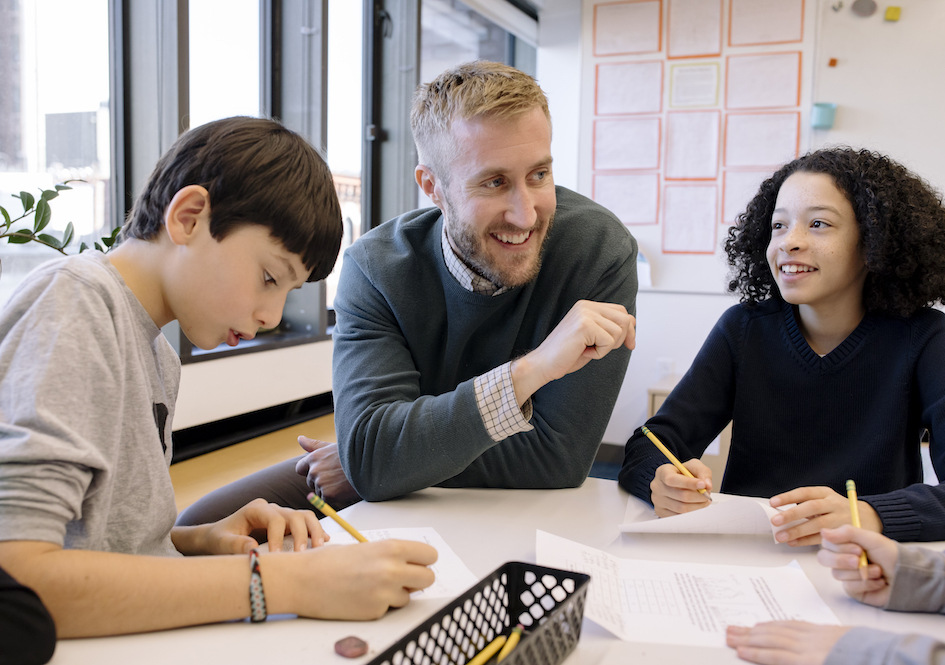 Two students writing at table with teacher