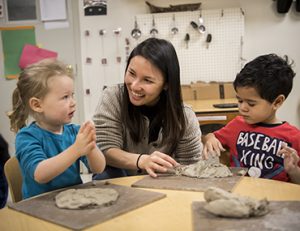 Teacher and two young children play with clay