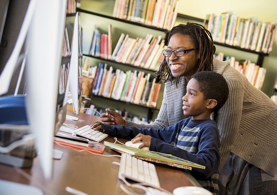 Teacher and child look at library computer