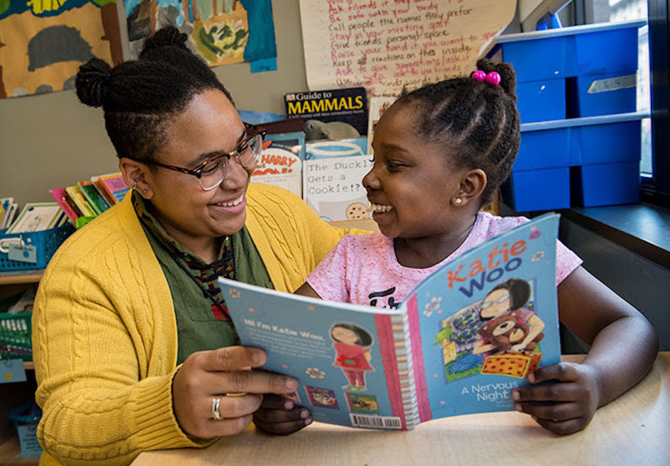 Child and teacher read a book together