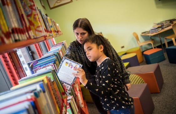 Teacher helping student pick out book in library