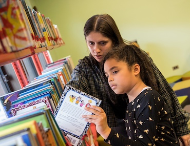 Teacher helping student pick out book in library