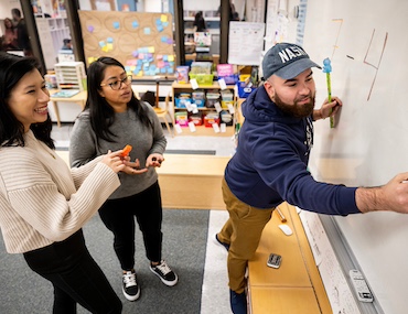 Teacher writes on whiteboard as two other teachers observe