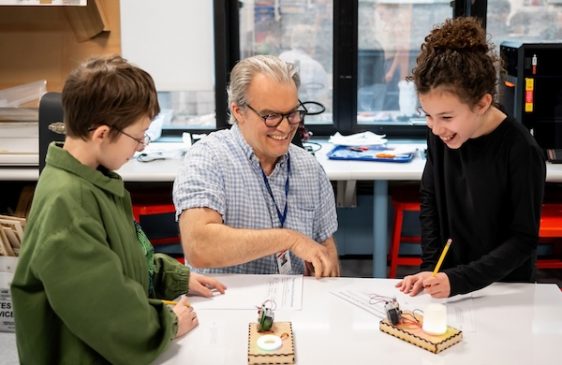 Teacher helps two students with science experiment