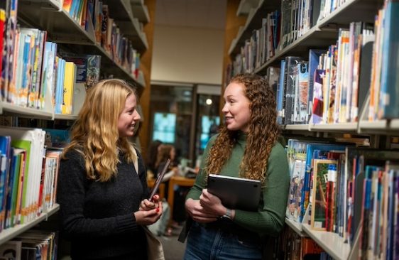 Two grad students in bookshelves in library