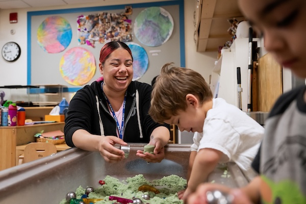 Teacher smiling with two students at sensory table