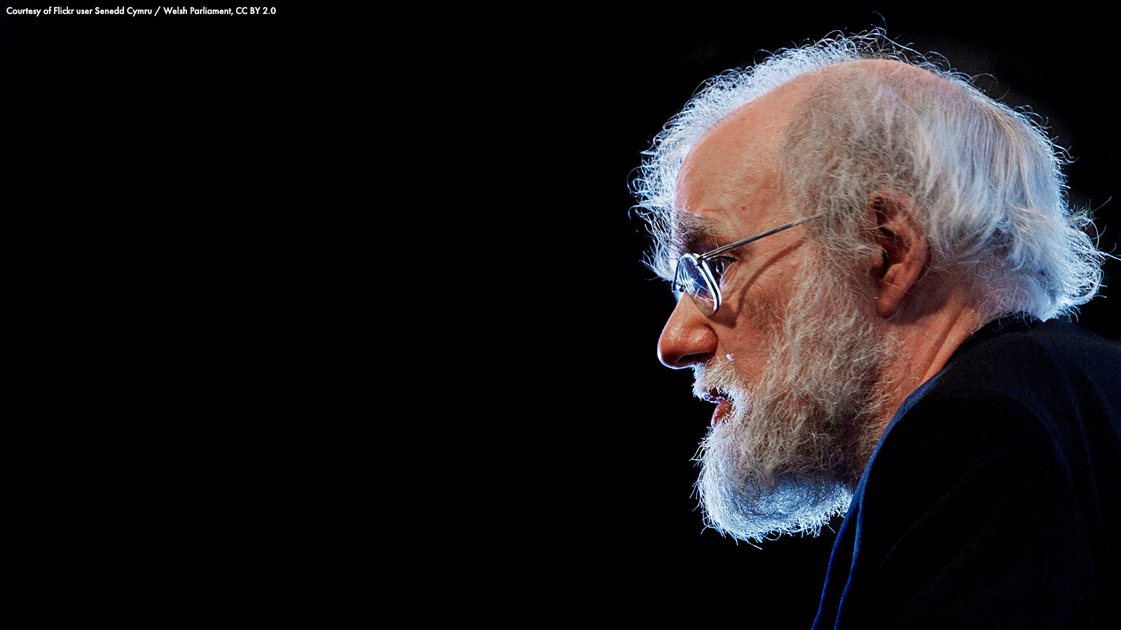 Rowan Williams' head silhouetted against a dark background. Via Flickr: Senedd Cymru / Welsh Parliament, CC BY 2.0.