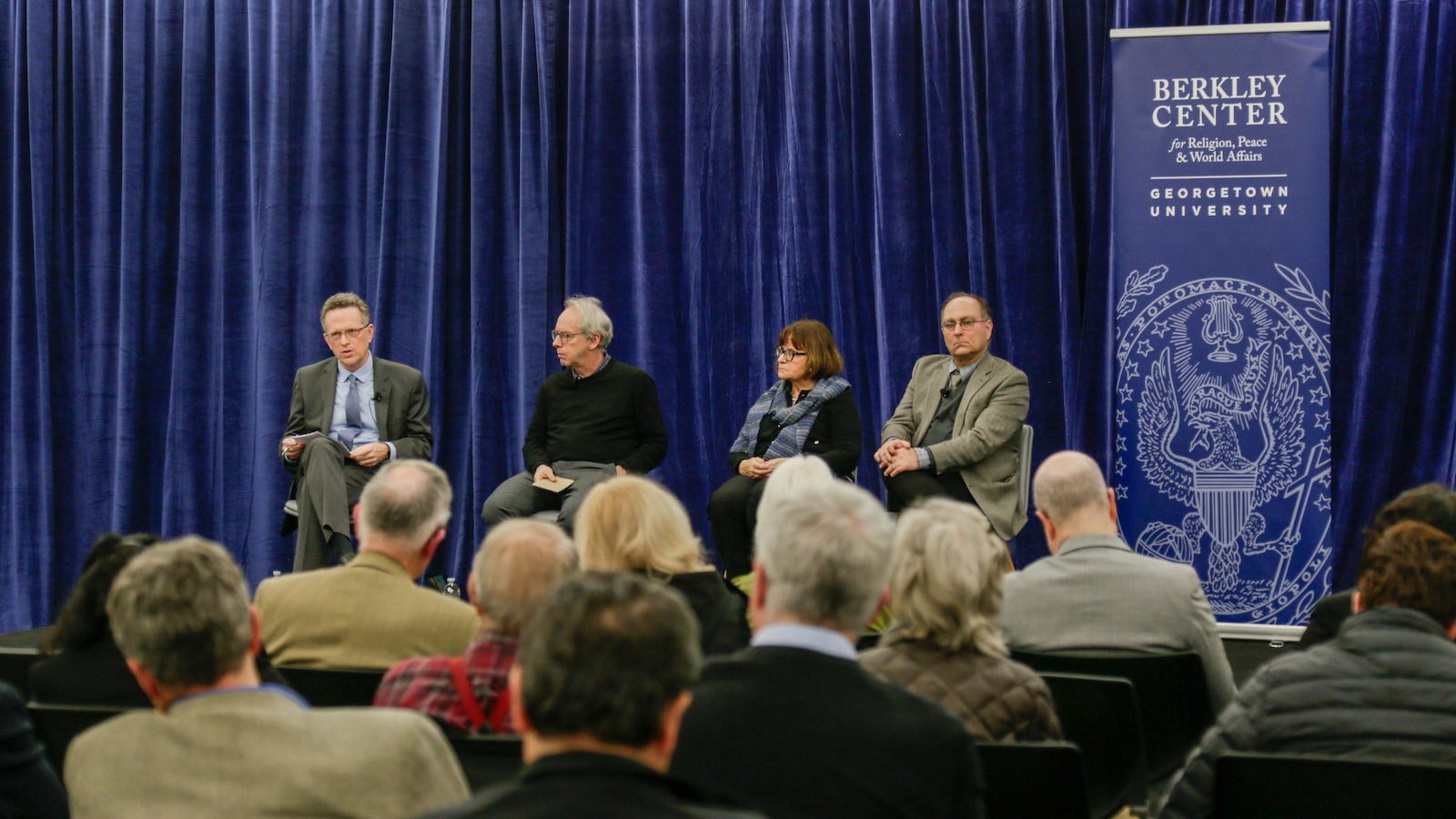 Panelists from the event sit on a stage in front of a crowd