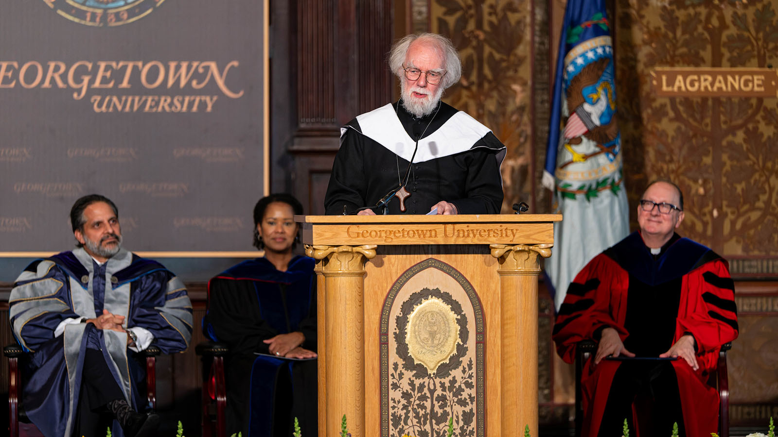 Rowan Williams stands at the podium in Gaston Hall with Georgetown leaders seated behind him. Photo by Phil Humnicky.