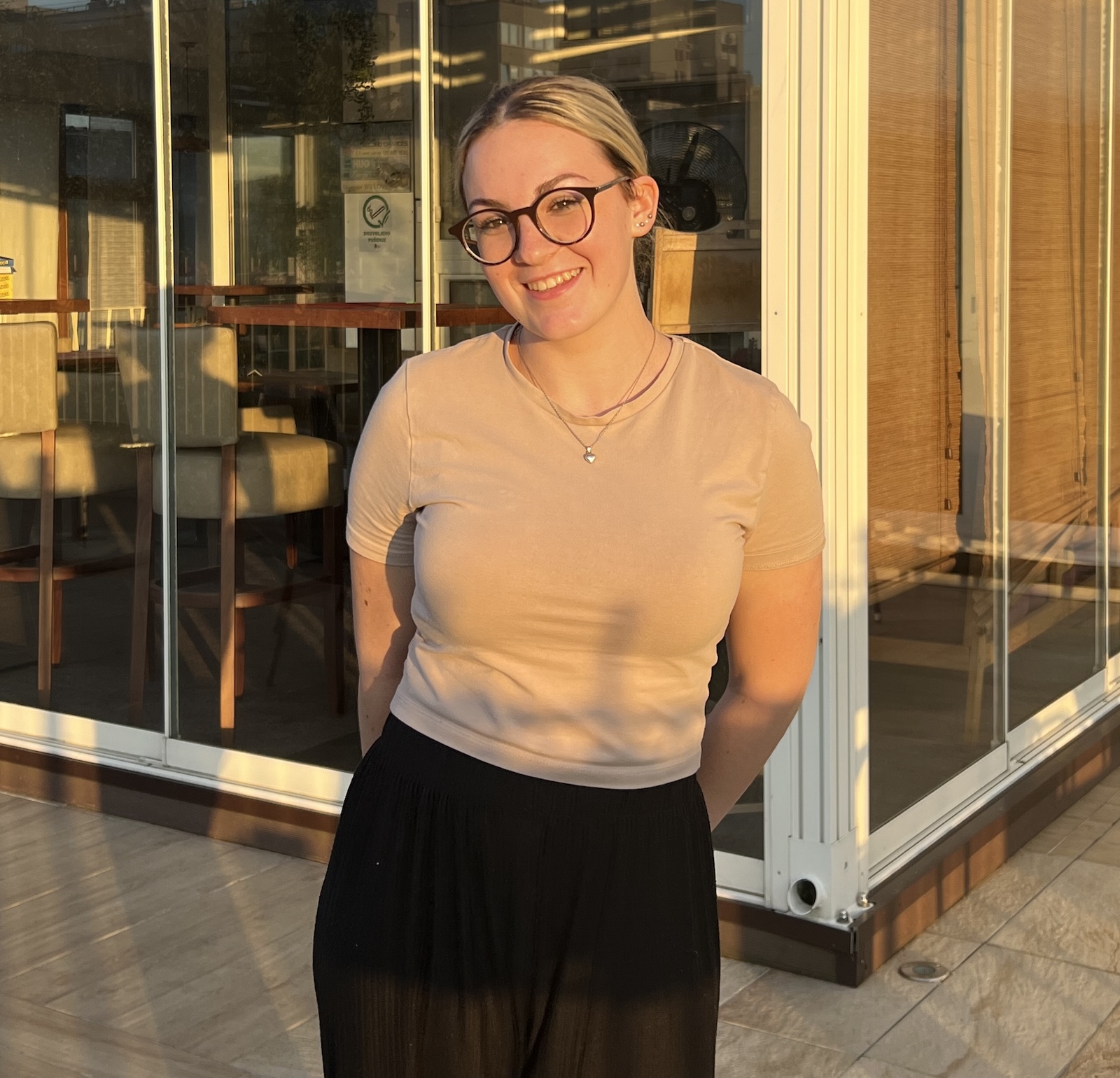 Ana stands outside in a a tan shirt and black skirt