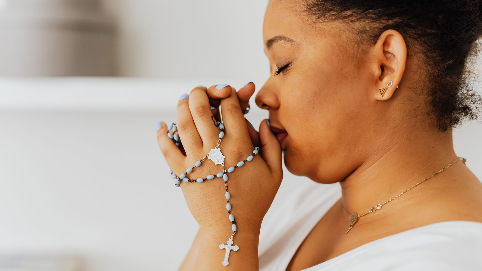 Black woman praying with folded hands while holding a rosary