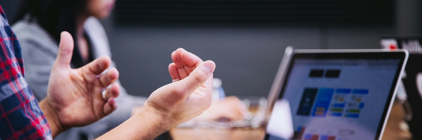 A person speaking at a meeting with a computer in front of them