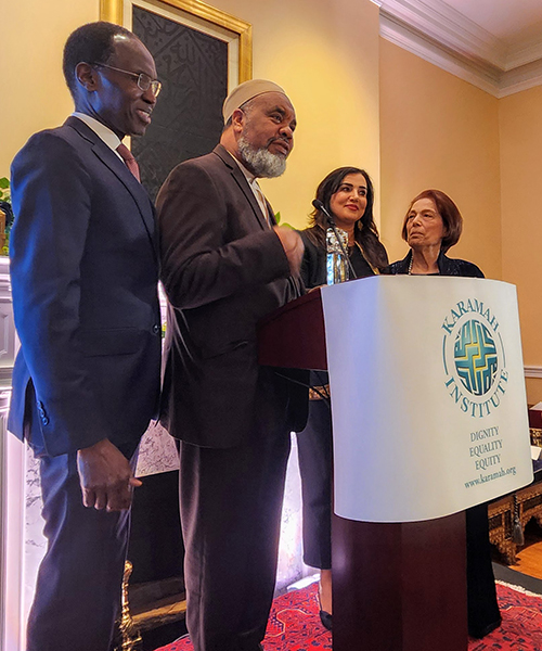Imam Mohamed Magid stands with others at a podium with a "Karamah Institute" sign