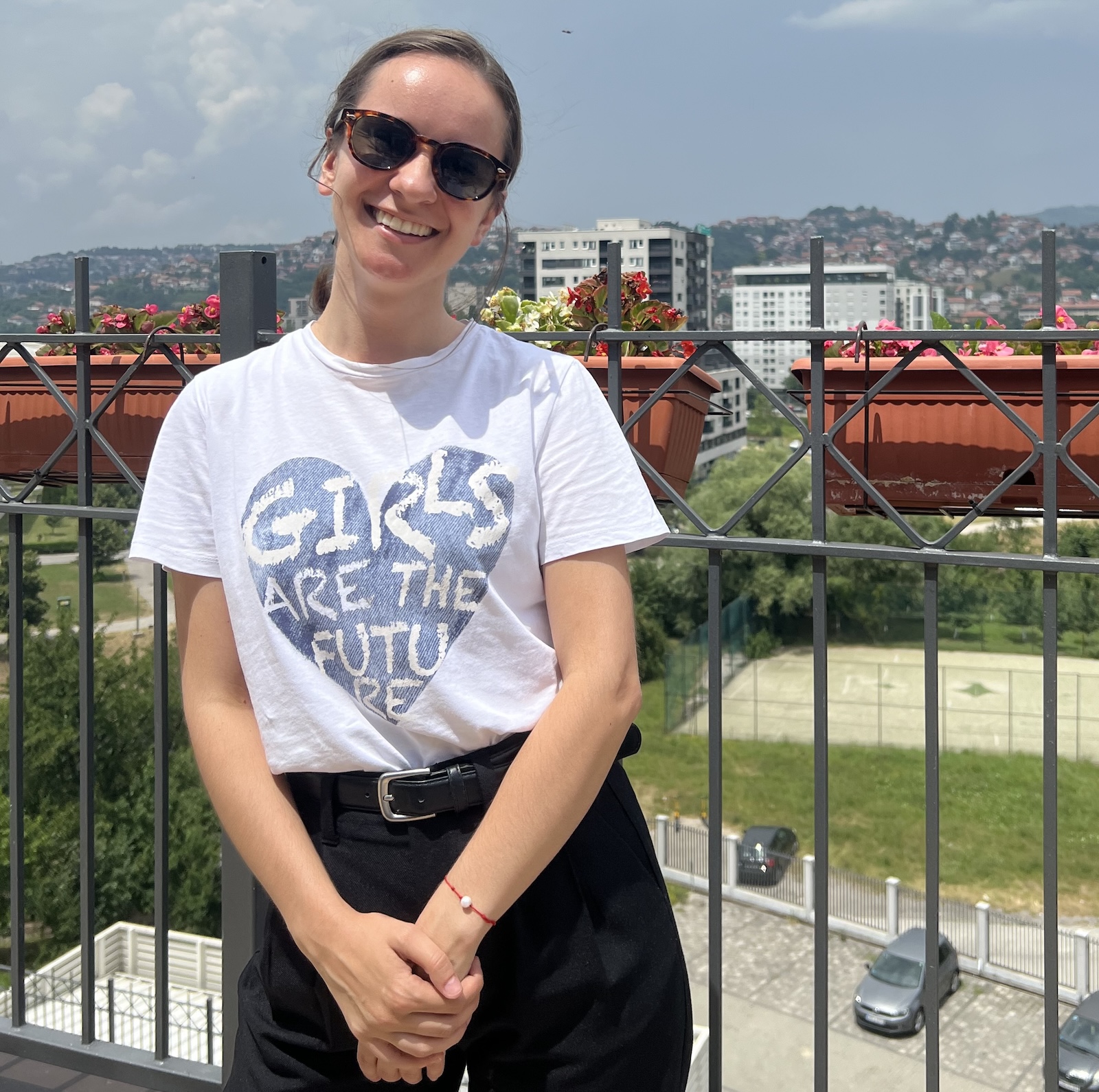 Martina stands outside in a T-shirt, black pants, and sunglasses
