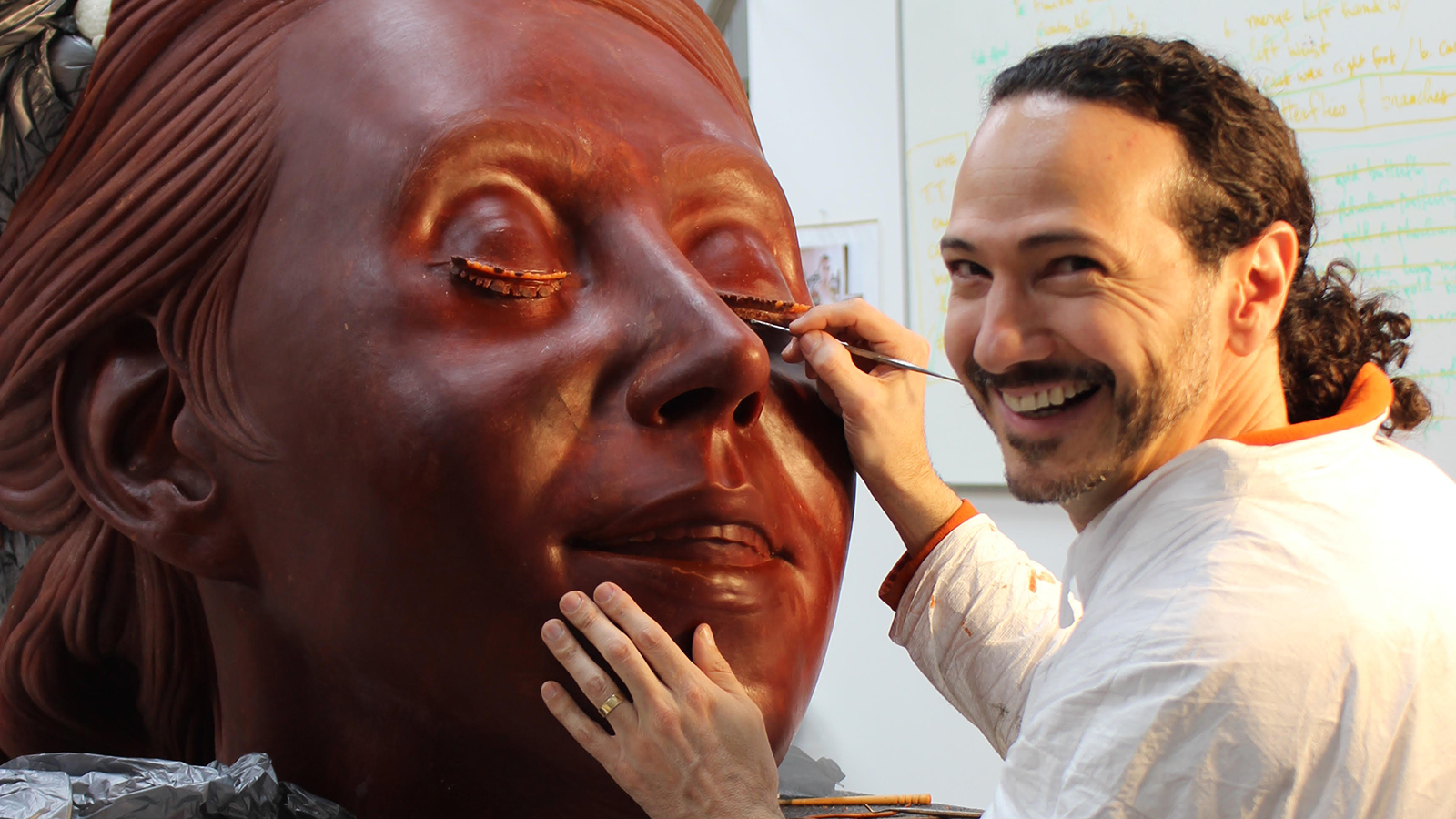 Patrick Beldio smiling while carving a large sculpture of a woman's head