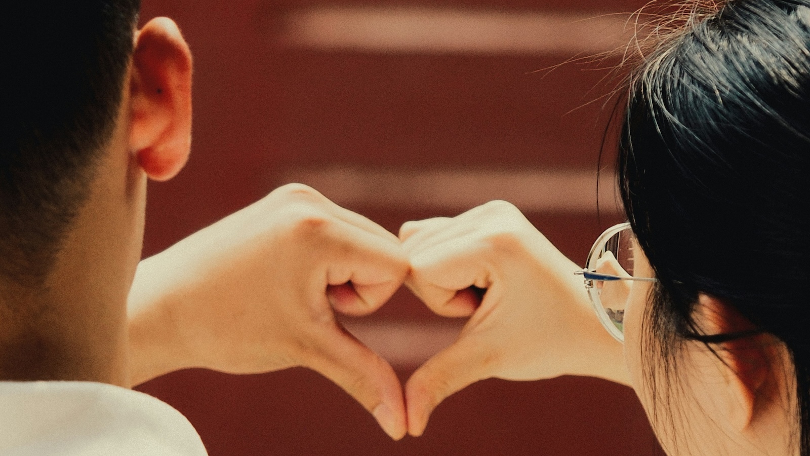 Two people standing next to each other and connecting their hands into a heart shape