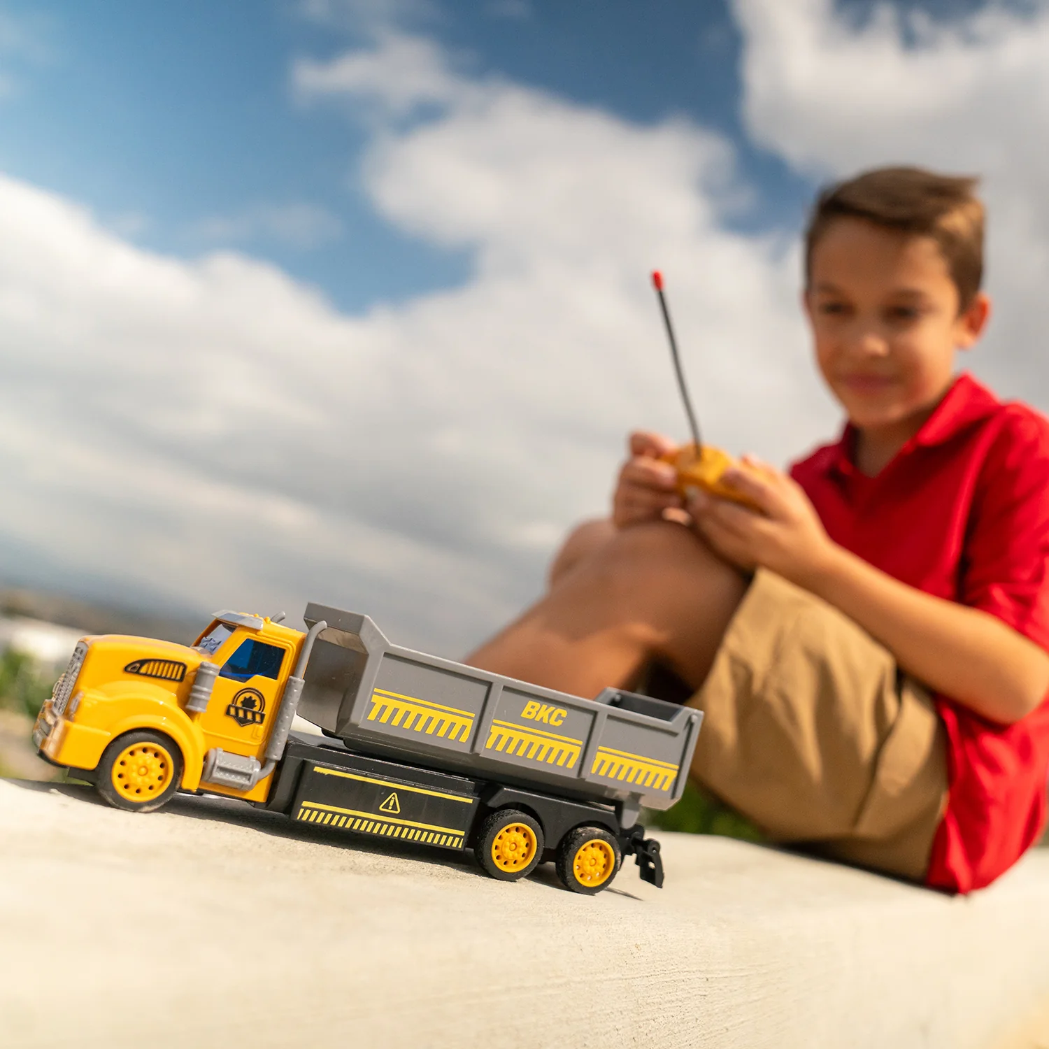 A boy controls a remote control construction truck outdoors on the beach.