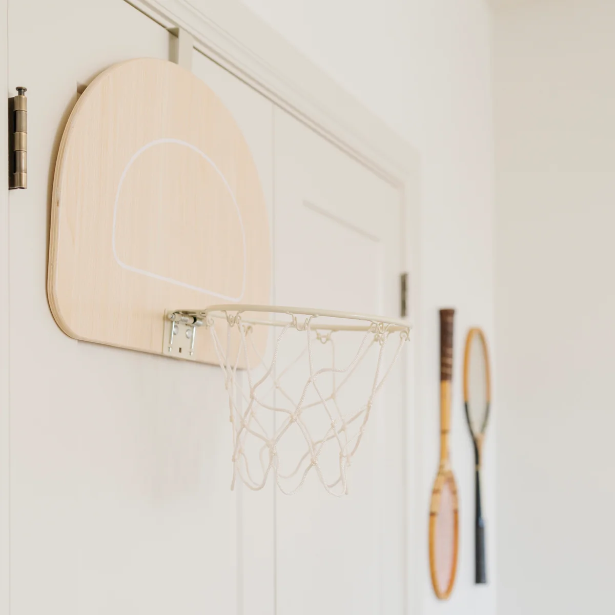 The white wooden style indoor door basketball stand is fixed on the top of the door, and a badminton racket is hung next to it.