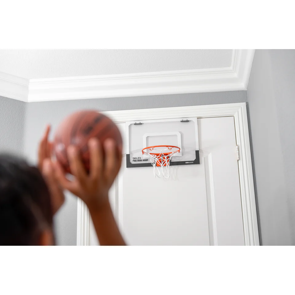 A boy holds a basketball, preparing to shoot, and a basketball net hangs above the white bedroom door.