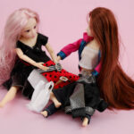 Two common plastic doll wigs for sale, with clothes piled up on a pink background.