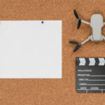 A cork background with a large white sheet of paper, a small drone (Best Drones for Cinematography), and a clapperboard placed on top.
