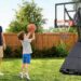 A cheerful father watching his young son practice a shot on a heavy-duty Yohood basketball goal with a foldable side frame system in a sunny backyard.