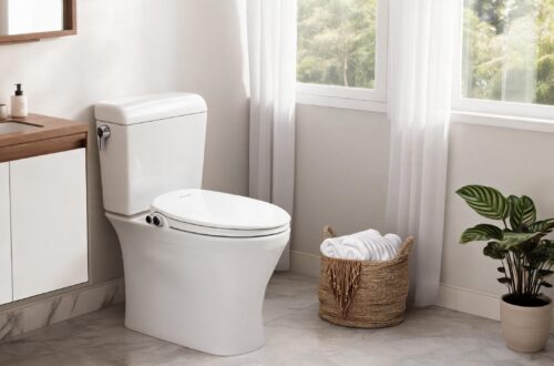 An elegant lifestyle image of a minimalist modern bathroom featuring a sleek toilet upgraded with a Brondell Swash white non-electric bidet seat next to a wicker towel basket and green plant.