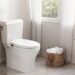 An elegant lifestyle image of a minimalist modern bathroom featuring a sleek toilet upgraded with a Brondell Swash white non-electric bidet seat next to a wicker towel basket and green plant.