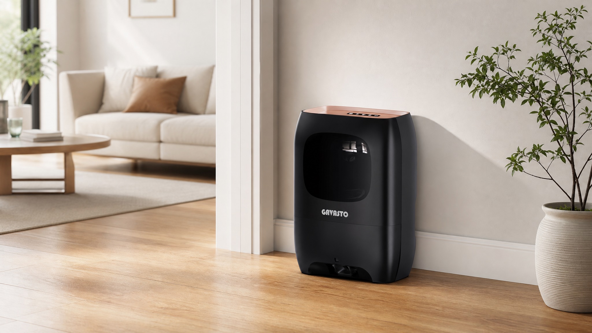 A sleek black GAVASTO touchless vacuum stationary automatic dustpan with a rose gold top accent, placed against a white wall on a light hardwood floor next to a potted plant.