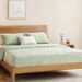 A minimalist Japanese-style wooden bedroom featuring an EGOHOME mattress with a light green quilted diamond pattern cover, decorated with matching green and white pillows for a natural, soothing atmosphere.