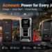 Lineup of ACMOUNT car jump starters and portable battery packs charging a smartphone, smartwatch, and laptop at an outdoor campsite with an off-road truck in the background.