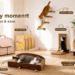 A warm living room displaying various FUKUMARU cat products, including a cat carrier, tofu cat litter, a cat scratcher bed sofa, an L-shaped vertical scratcher, a 5-in-1 scratcher box, and wall-mounted climbing steps with cats actively playing.