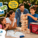 Family playing Giantville giant tumbling blocks at an outdoor game night, with a wooden tower, Family Fun Pack cards, activity sheets, large wooden die, and red carry bag for interactive indoor and outdoor play.