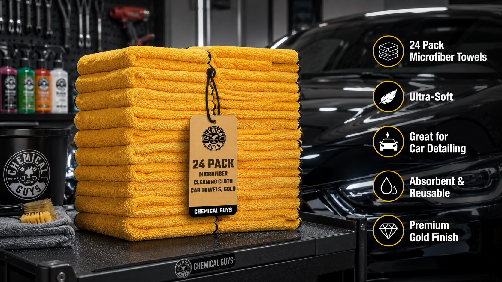 A tall stack of plush yellow microfiber cleaning towels with a black hanging tag labeled "24 PACK MICROFIBER CLEANING CLOTH" from Chemical Guys, set on a garage workbench with a blurred black car and tools in the background.