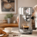 Woman uses a silver espresso machine to brew espresso and steam milk in a warm sunlit kitchen, with coffee beans, croissants and prepared lattes creating an inviting home café atmosphere.