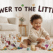 A wide shot of a smiling baby with curly hair sitting on a shaggy rug in a living room, surrounded by multiple Serenity Kids baby food pouches of different flavors like Beef, Chicken, and Bison, and several plush lamb and rabbit toys. Across the top, the text "POWER TO THE LITTLES" is written with small animal illustrations. A pink text box in the bottom left corner reads "Big Nutrition for Little Explorers".