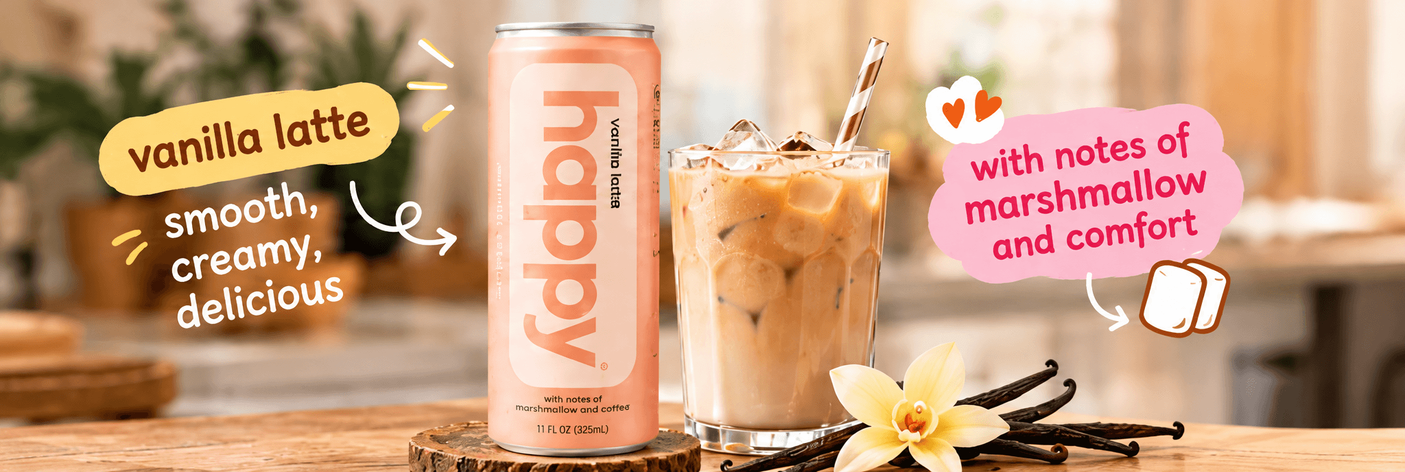 Alt (EN) A peach happy "vanilla latte" can (11 FL OZ / 325 mL, labelled "with notes of marshmallow and coffee") standing on a round wooden trivet, next to a highball glass of iced vanilla latte with a striped straw, with a vanilla blossom and vanilla pods in the foreground. Hand-drawn callouts read "vanilla latte", "smooth, creamy, delicious" and "with notes of marshmallow and comfort", set against a warmly blurred home-kitchen counter.